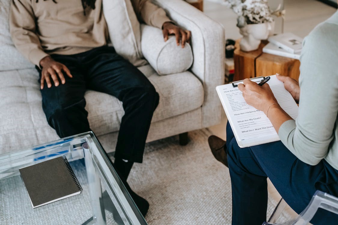Patient sitting on couch talking to therapist in chair while therapist is writting