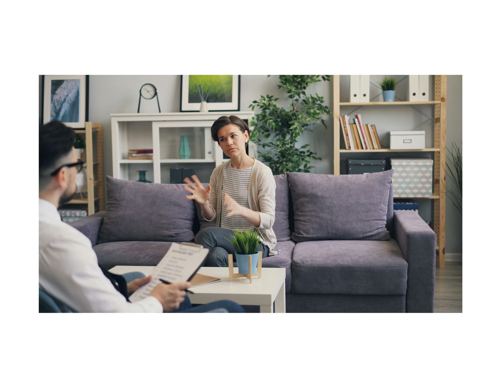 a psychologist sitting in a chair with a notepad talking with a woman sitting on a couch in a nice office